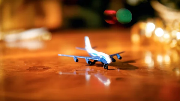 Closeup image of miniature toy airplane against glowing Christmas lights. Concept of winter holidays travelling — Stock Photo, Image