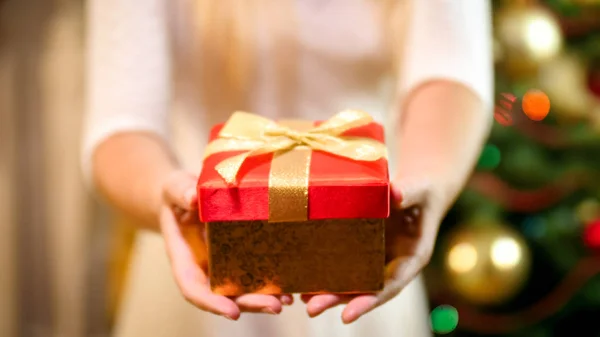 Imagem de close-up da jovem mulher com caixa de presente de Natal em pé na árvore de Natal — Fotografia de Stock