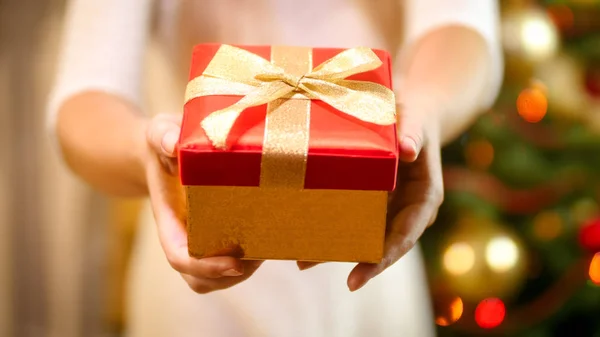 Imagen de primer plano de la mujer joven que muestra la caja de regalo de Navidad con arco dorado en la cámara —  Fotos de Stock