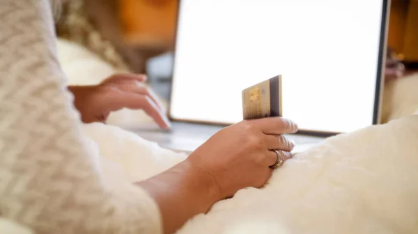 Närbild bild av ung kvinna håller bank kreditkort och gör online shopping i sängen — Stockfoto