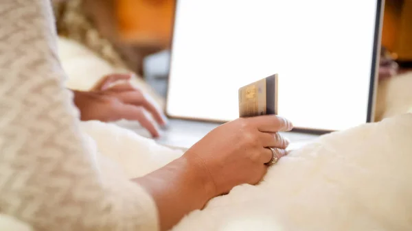 Closeup image of young woman with credit card lying in bed and browsing online store on laptop — Stock Photo, Image
