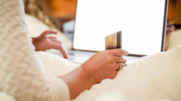 Imagen de primer plano de la mujer sosteniendo la tarjeta de crédito mientras está acostado en la cama y navegar por las ventas en línea en las tiendas —  Fotos de Stock