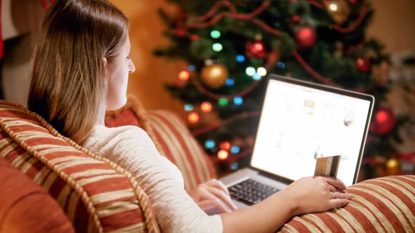 Jovem mulher sentada em poltrona na véspera de cristmas e fazendo compras online — Fotografia de Stock