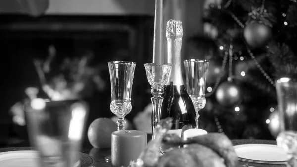 Imagem em preto e branco da garrafa de champanhe e copos contra a árvore de Natal decorada — Fotografia de Stock