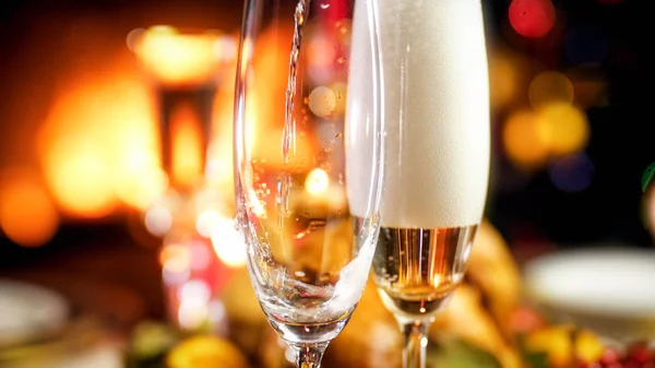 Closeup image of champagne flowing in two glasses against burning fireplace — Stock Photo, Image