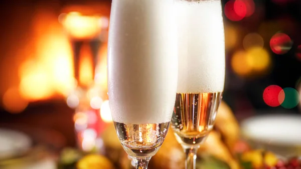 Closeup image of bubbles and foam in glasses of champagne against burning fireplace and Christmas tree — Stock Photo, Image