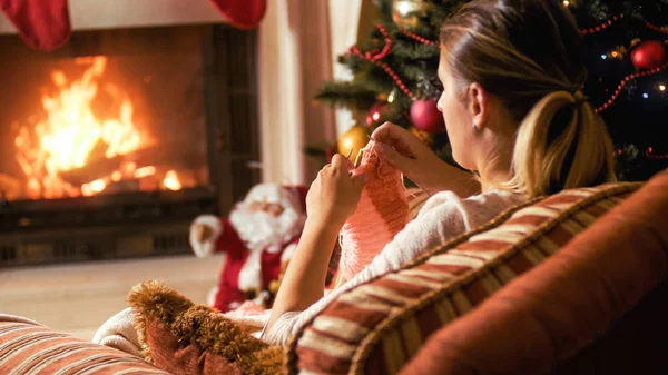 Retrato tonificado de mujer joven tejiendo calcetines en sillón y mirando a la chimenea ardiente — Foto de Stock