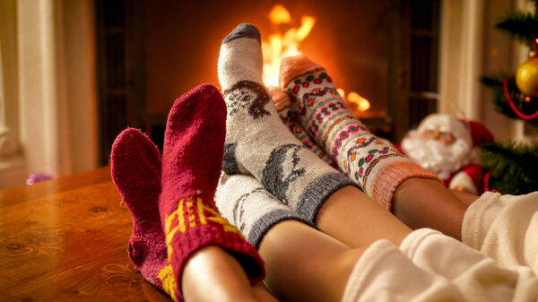 Family wearing warm knitted socks relaxing at house with burning fireplace