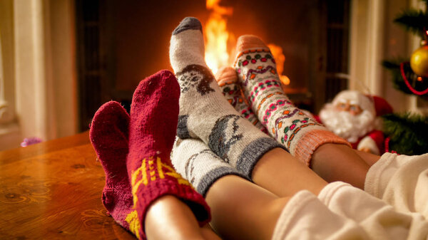 Closeup image of three persons in knitted woolen socks warming at the fireplace in chalet