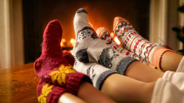 Closeup image of mothers, fathers, and childs feet in woolen socks lying next burning fireplace