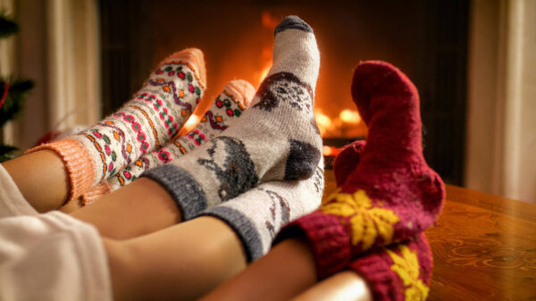 Closeup image of family feet in warm knitted socks lying next to burning fireplace in living room