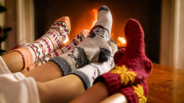 Imagen de tres personas en calcetines de punto de lana calentándose junto a la chimenea en llamas —  Fotos de Stock