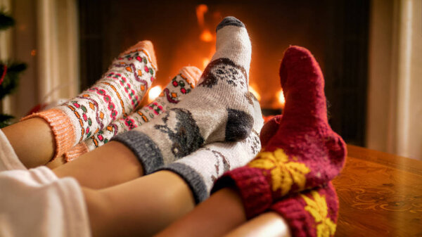 Closeup image of young family in knitted woolen socks lying under blanket and warming by the burning fire