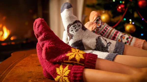Familj i ylle strumpor hålla fötterna på träbord bredvid brinnande spis och julgran — Stockfoto