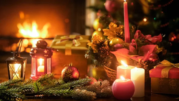 Closeup image of traditional Christmas decorations and candles on wooden table against fireplace — Stock Photo, Image