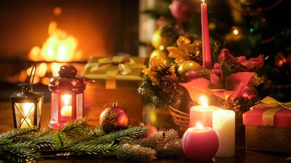 Beautiful christmas background with candles and lanterns on wooden table against burning fireplace — Stock Photo, Image