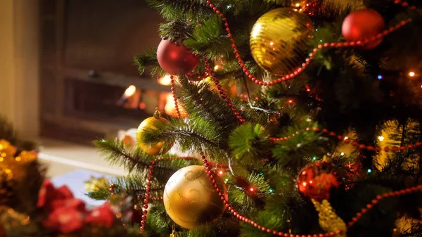 Immagine primo piano di bagattelle e luci colorate sull'albero di Natale contro il camino in fiamme — Foto Stock