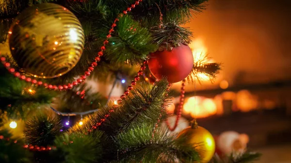 Immagine di primo piano di belle bagattelle appese all'albero di Natale decorato contro il camino ardente a casa — Foto Stock