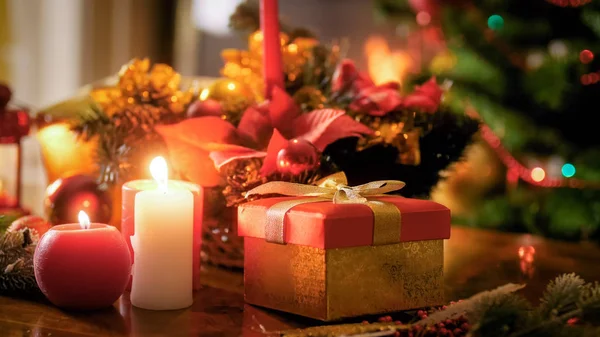 Closeup image of burning candles standing against gift box and Christmas tree — Stock Photo, Image