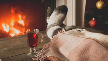 Toned image of woman in woolen socks lying under blanket and drinking tea at burning fireplace clipart
