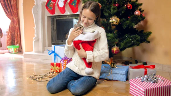 Hermosa chica adolescente morena con gatito sentado bajo el árbol de Chrismta en la sala de estar —  Fotos de Stock