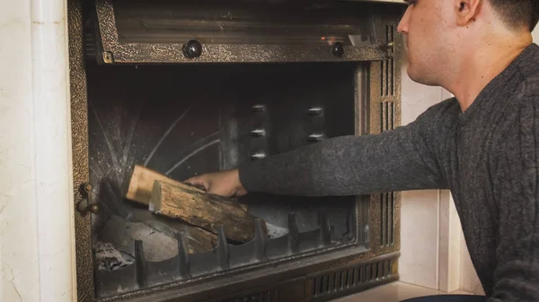 Porträt eines jungen Mannes, der Holzscheite in Kamin auf Wohnzimmer wirft — Stockfoto