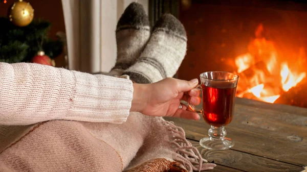 Imagen de primer plano de la mujer en calcetines de lana junto a la chimenea y beber té caliente — Foto de Stock