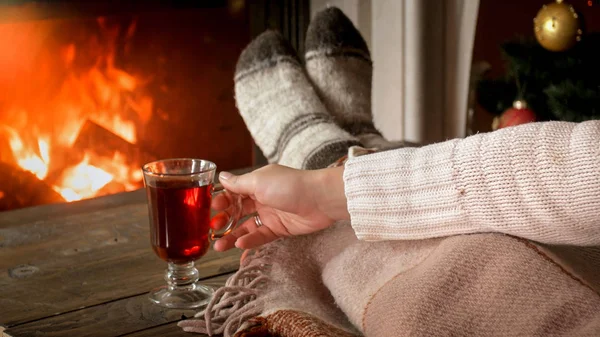 Foto de primer plano de la mujer joven calentando con té caliente en la sala de estar con chimenea ardiente — Foto de Stock