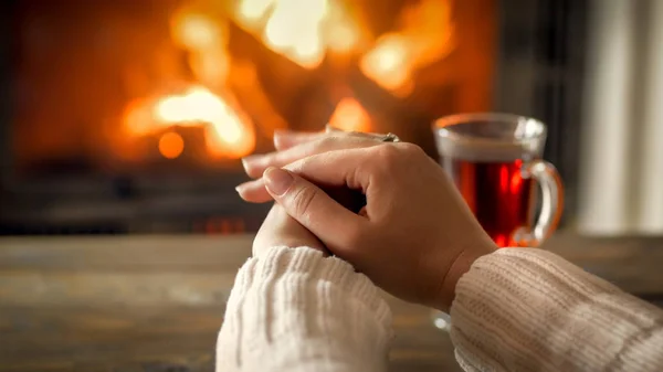 Closeup image of youn g woman in sweater warming hands by the fireplace — Stock Photo, Image