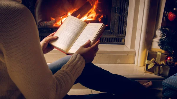 Imagen tonificada de una joven leyendo un libro junto a la chimenea en la víspera de Navidad — Foto de Stock