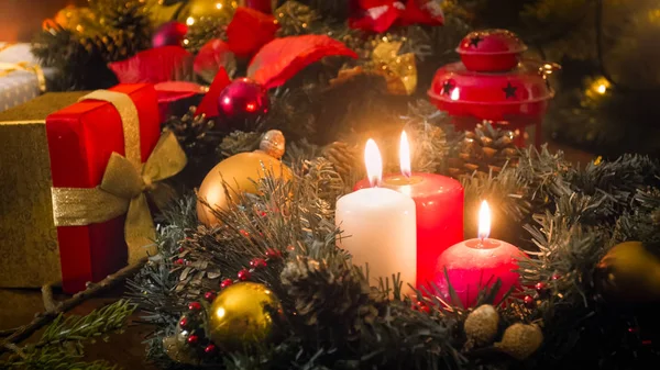 Imagen tonificada de tres velas encendidas, regalos y corona de flores en la víspera de Navidad — Foto de Stock