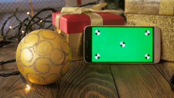 Imagens de close-up 4k da câmera lentamente se debruçando sobre a mesa de madeira com decorações de Natal e smartphone. Exibição de chromakey verde para inserir sua imagem ou vídeo na tela — Vídeo de Stock