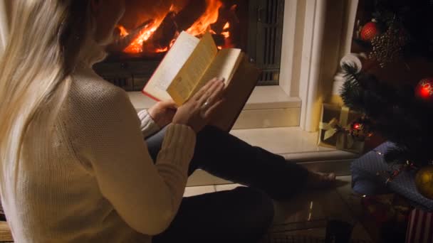 4k video de mujer joven leyendo libro y beber té junto al árbol de Navidad y chimenea en la noche — Vídeos de Stock