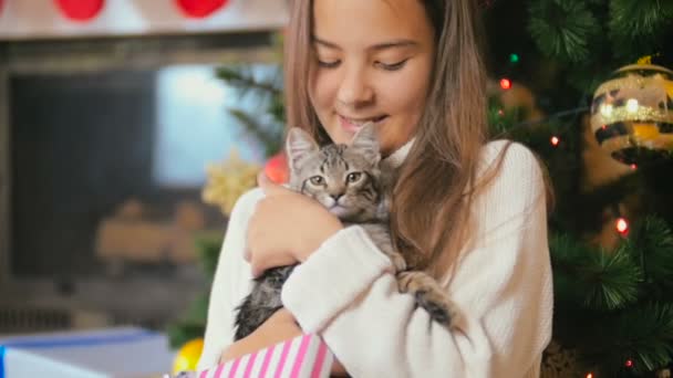 Τονισμένο αργή κίνηση μήκος σε πόδηα του χαμογελαστό κορίτσι χαϊδεύει και Αγκαλιάζοντας το γατάκι στο σαλόνι διακοσμημένο για τα Χριστούγεννα — Αρχείο Βίντεο