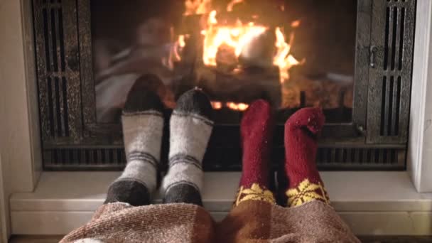 恋の燃える暖炉のそばで横になっているニットの暖かい靴下を身に着けているカップルのスローモーション映像 — ストック動画