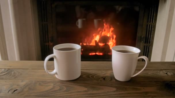 Imágenes en cámara lenta de dos tazas con té ot contra la chimenea en la sala de estar — Vídeo de stock