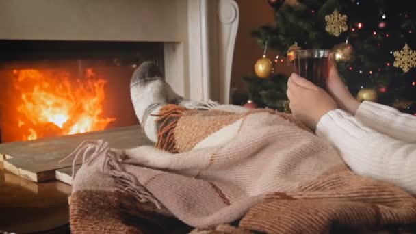 Stonowanych wideo kobietę leżącą na kanapie obok kominki i picie herbaty w Wigilię Bożego Narodzenia — Wideo stockowe
