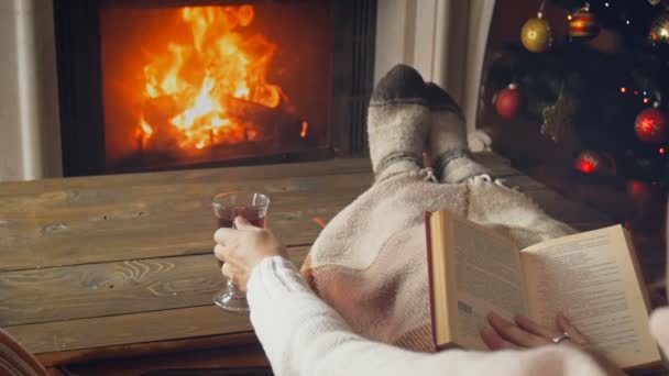 SLow motion footage of woman reading book and drinking tea next to burning fireplace on Christmas eve — Stock Video