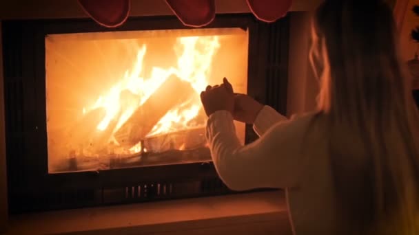 Images au ralenti de la jeune femme assise près de la cheminée en feu et se réchauffant les mains — Video