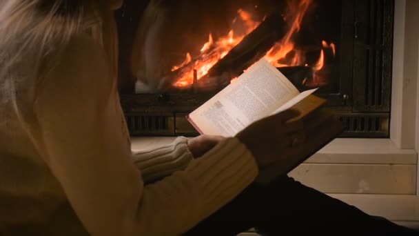 Медленное движение видео красивой женщины oyung чтение книги ночью при свете от горящего камина — стоковое видео