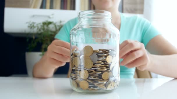 4 k video van jonge vrouw schrijven besparingen op glazen pot vol munten — Stockvideo