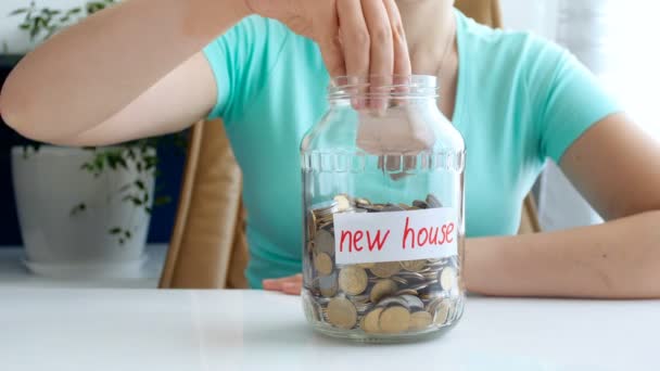 4k vídeo conceptual de la mujer joven recogiendo y ahorrando dinero para la nueva casa. Pequeña casa de juguete appeairng en la mesa — Vídeos de Stock