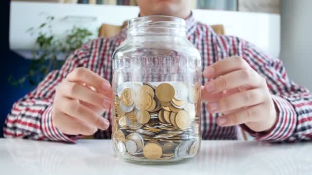 Closeup 4k beelden van jonge man gooien van munten in moneybox jabeled besparingen — Stockvideo