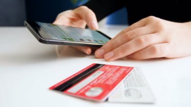 Genç kadın Smartphone cep telefonu ile online mağazalar tarama portre görüntüleri. Onun yanındaki masada yatan iki kredi kartları.