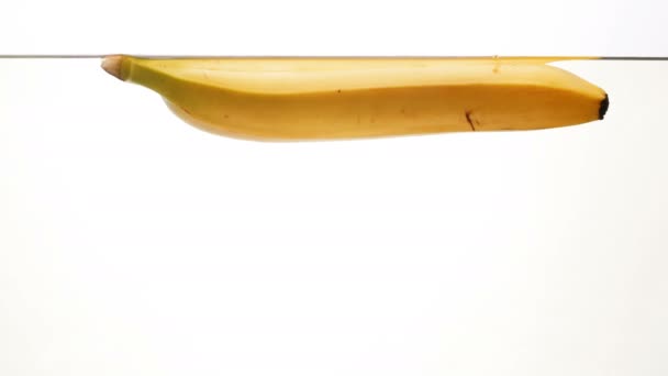 Closeup 4k πλάνα του ώριμη μπανάνα που επιπλέει στο νερό εναντίον λευκό backgorund — Αρχείο Βίντεο