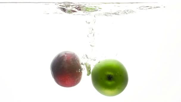 Крупный план замедленной съемки свежего зеленого и красного яблока, падающего в холодной воде на белом фоне — стоковое видео