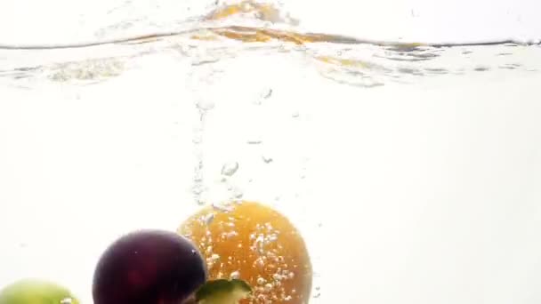 Primer plano imágenes en cámara lenta de frutas tropicales jugosas frescas cayendo y salpicando en agua fría y clara sobre fondo blanco. Nutrición saludable y vitaminas — Vídeo de stock