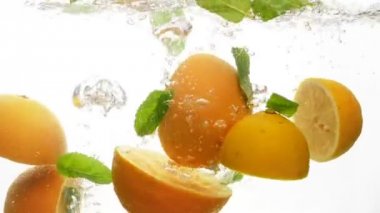 Closeup ağır çekim görüntüleri düşen suya sulu ve olgun narenciye. Portakal ve limon nane ile yarısı yaprakları suda sıçraması
