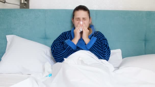 Vídeo 4k de una joven enferma acostada en la cama, usando pañuelos de papel y aplicando aerosol nasal — Vídeo de stock