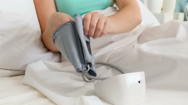 Primer plano 4k video de una joven enferma acostada en la cama y midiendo la presión arterial — Vídeos de Stock
